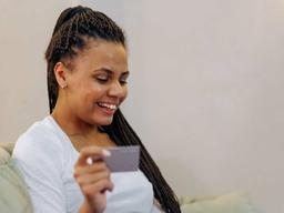 Imagem de uma mulher usando o cartão de crédito e sorrindo. Usamos a foto para ilustrar o post que discute o que acontece quando alguém pagar metade da fatura do cartão