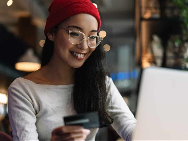 Imagem de uma mulher usando um computador e seu cartão de crédito enquanto provavelmente faz uma pesquisa, usamos a foto para simbolizar o post sobre melhores cartões de crédito sem anuidade