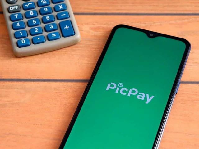 Imagem de um celular com a logo do PicPay ao lado de uma calculadora. Foto utilizada para ilustrar uma notícia sobre a cobrança da taxa do PicPay. Crédito: Shutterstock.