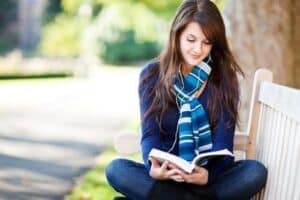 Moça lendo livro no parque tentando aprender mais sobre educação financeira