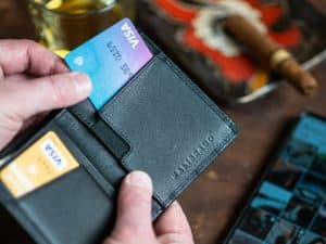 Imagem aproximada de uma mão, aparentemente masculina, segurando uma carteira preta com vários cartões de crédito. Usamos a foto para ilustrar o post sobre a fatura do cartão Avista