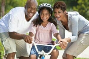 Casal ensinando a filha a andar de bicicleta simbolizando o tema Planejamento para ter um filho
