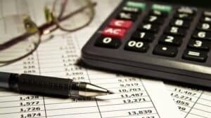 Entenda, de uma vez por todas, a diferença entre despesas fixas e variáveis Óculos, calculadora, caneta e um papel para analisar despesas fixas e variáveis