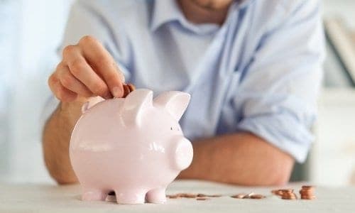 Estabeleça uma meta de poupança homem botando moedas em um cofre de porquinho