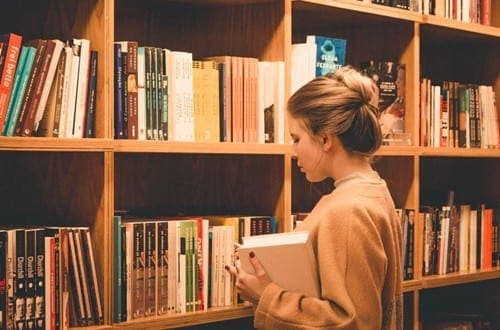 mulher segurando um livro em frente a uma estante enorme de livros