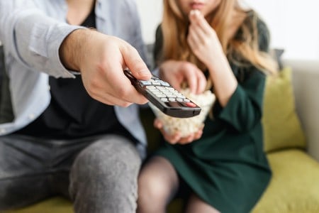 Imagem de um casal vendo televisão, item da casa que pode representar economia de energia