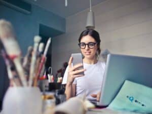 Imagem de uma mulher em seu escritório usando o computador e o celular, entendendo como montar um pequeno negócio