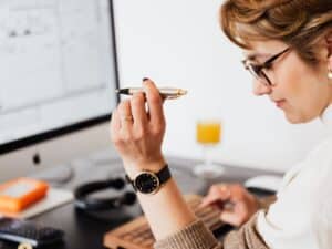 Imagem de uma mulher usando o computador e uma caneta para entender como sair das dívidas rapidamente