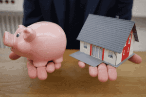 Pessoa segurando cofrinho e miniatura de casa simbolizando o tema Pagar menos juros no financiamento imobiliário