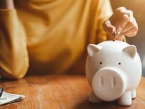 mulher colocando moedas em um porquinho para simbolizar o tema: começar a guardar dinheiro