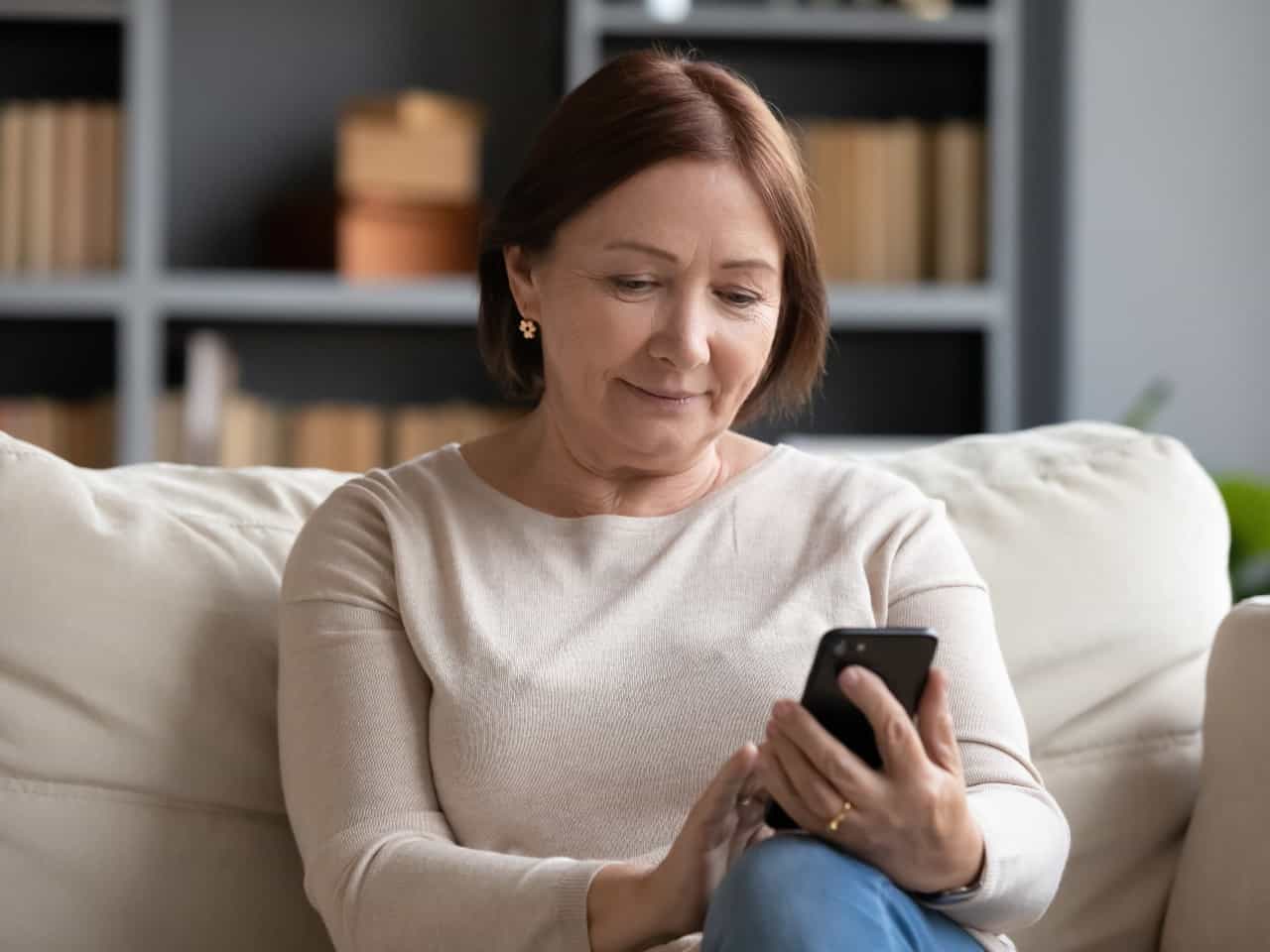Imagem de uma mulher usando o seu celular sentada no sofá. Usamos a imagem para ilustrar o conteúdo sobre o cálculo de FGTS