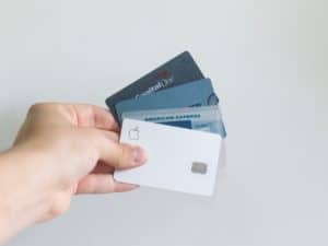 Imagem de uma mão segurando quatro cartões de crédito nas cores branca, azul e cinza. A foto foi usada para ilustrar o conteúdo do iDinheiro sobre como funciona o parcelamento da fatura do cartão de crédito.