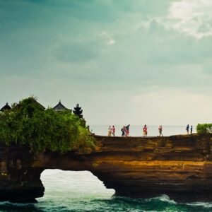 paisagem da Indonésia em que aparece o mar e uma espécie de ponte com turistas. Do lado esquerdo há vegetação e apenas o topo de construções em estilo indonésio
