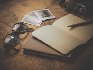 um óculos com fotos ao lado e um caderno com lápis. No fundo, um mapa, que simboliza uma pesquisa por um destino para viajar