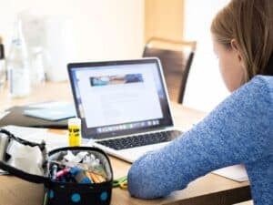 menina de costas olhando para uma tela de computador para estudar com materiais de escola ao seu lado, como cola, lápis, estojo e mais