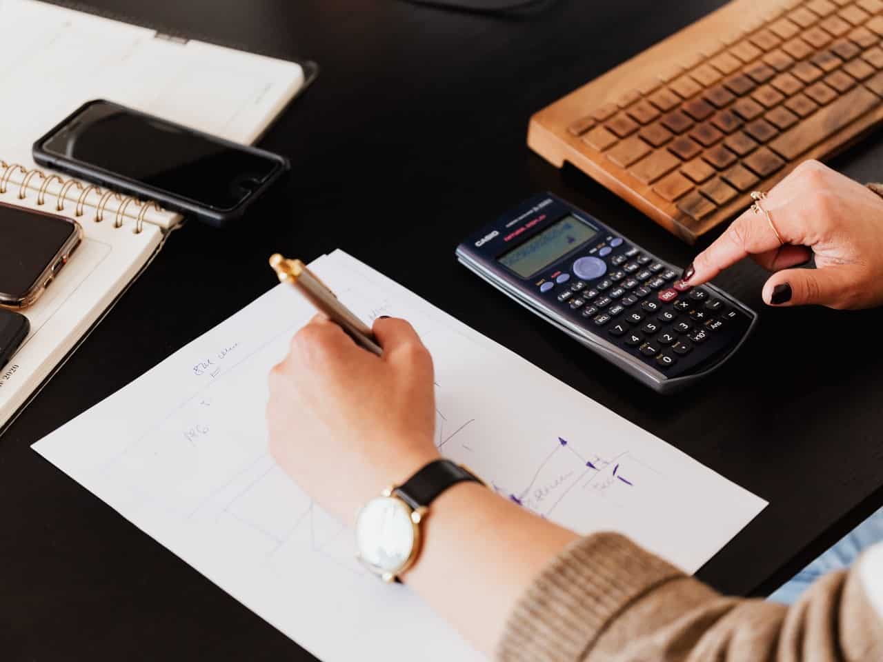 Imagem de uma pessoa usando sua mesa de trabalho com um papel e calculadora para ilustrar o conteúdo da Calculadora de Custo de Funcionário para Empresa