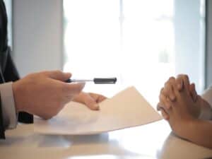 Homem de terno entregando uma caneta e um contrato para outra pessoa que quer contratar um empréstimo pessoal para negativado