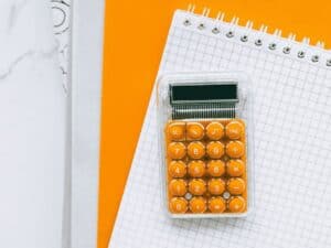 calculadora laranja em cima de papéis, representando icms na base do pis