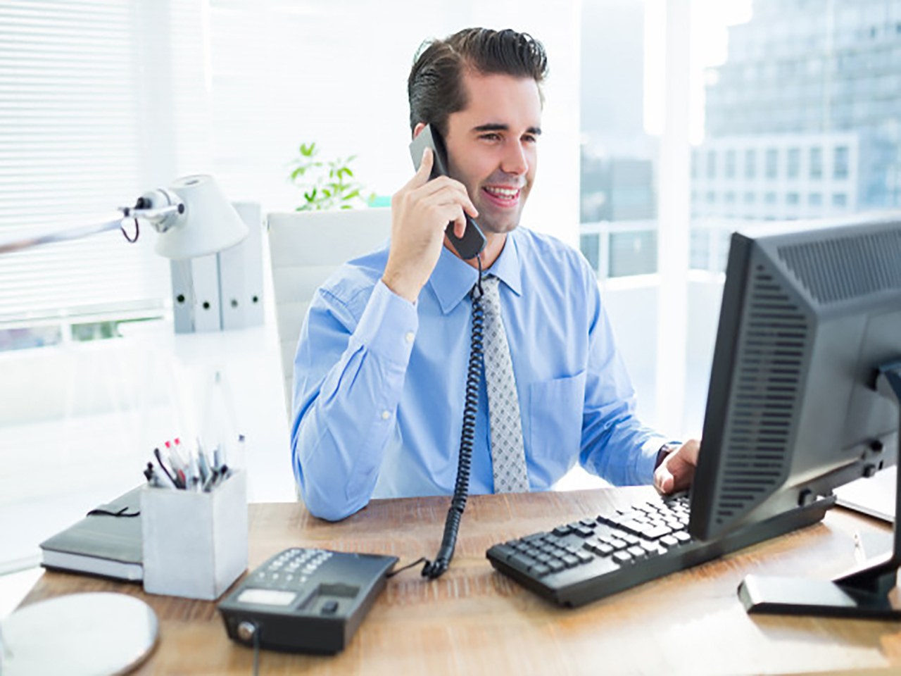 imagem de um homem falando ao telefone enquanto usa o computador para ilustrar o conteúdo sobre o bradesco net empresas