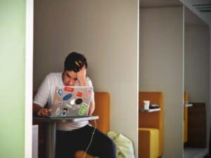homem sentando em uma poltrona, olha frustrado para a tela de um notebook. a imagem representa golpe virtual na pandemia