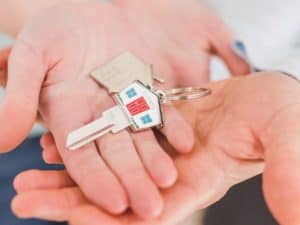 Imagem de duas pessoas segurando uma chave de casa em sua mão, representando nosso conteúdo sobre compra da casa própria