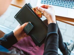 pessoa sentada retirando cartão de carteira com notebook ao fundo representando mudar de banco