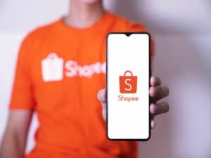pessoa com camisa da Shopee segurando celular com tela aberta na Shopee representando programa de afiliados da Shopee