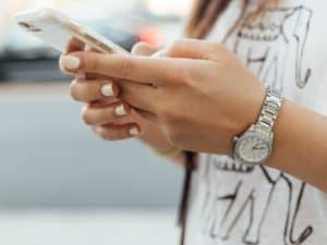 Imagem de uma mulher usando um relógio e blusa branca segurando um celular. A foto está centralizada nas mãos da pessoa e foi usada para ilustrar o nosso post que ensina como desbloquear o chip da Claro