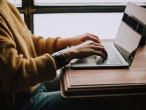Imagem de uma pessoa usando um suéter marrom, em um escritório, usando um laptop preto. Foto usada para ilustrar o post que avalia se a Americanet é boa