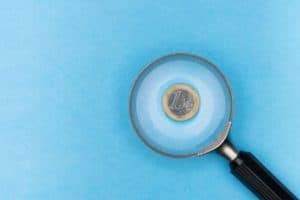 Uma lupa direcionada a uma moeda em um fundo azul