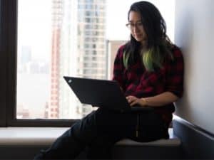 imagem de uma mulher sentada em uma janela com o computador no colo para o artigo sobre Vantagens de ser MEI!