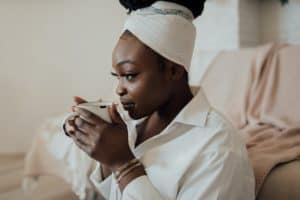 [seguro de vida mulher] uma mulher negra sentada, segurando uma xícara nas mãos, próxima ao rosto