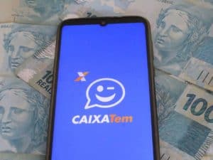 Imagem do aplicativo Caixa Tem e algumas notas de 100 reais. Imagem utilizada para ilustrar a notícia sobre o novo microcrédito digital Caixa.