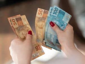 Imagem de duas mãos segurando notas de 50 e de 100 reais. Imagem utilizada para ilustrar uma notícia sobre o saque do fgts nascidos em janeiro
