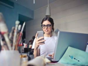 Imagem de uma mulher usando um computador enquanto olha seu celular. Foto usada para ilustrar nosso conteúdo sobre Portabilidade empréstimo consignado bxblue