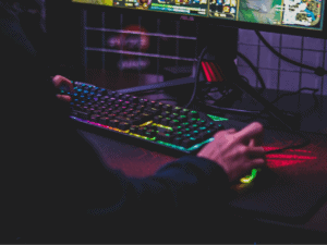 Imagem de uma pessoa jogando jogos em um computador gamer, com o teclado colorido e luz neon. Foto usada para ilustrar o conteúdo sobre consórcio gamer