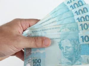 Imagem de uma mão segurando algumas cédulas de 100 reais. Imagem utilizada para ilustrar uma notícia sobre o saque extraordinário do FGTS. Fonte: Freepik .