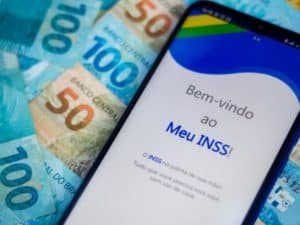 Imagem de um celular com o aplicativo do Meu INSS e algumas cédulas de 50 e 100 reais. Imagem utilizada para ilustrar uma notícia sobre o pagamento da segunda parcela do 13º do INSS.