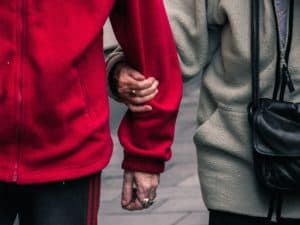 Imagem de um casal de idosos andando na rua com as mãos dadas. Um usa vermelho e outro cinza. Foto usada para ilustrar nosso post sobre o décimo quarto salário