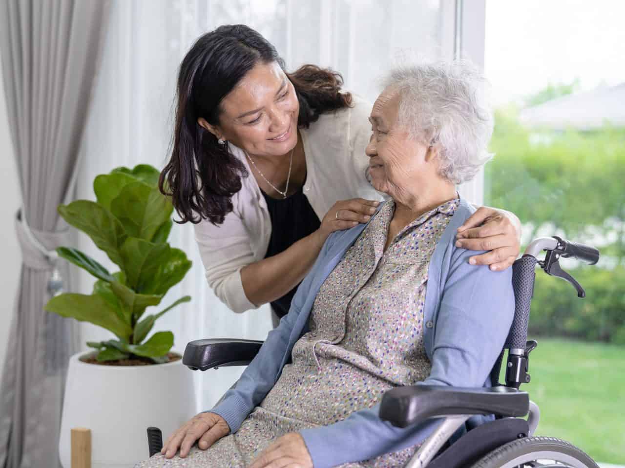 Mulher cuidando de uma idosa de cadeira de rodas.