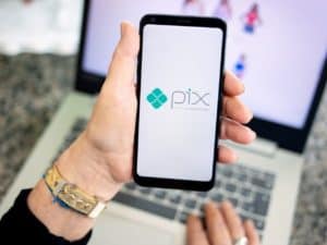 Imagem de um celular com a logo do PIX e um computador. Foto utilizada para ilustrar uma notícia sobre o PIX parcelado no cartão.