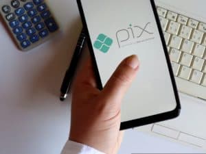 Imagem de um celular com a logo do PIX, ao lado de uma caneta, uma calculadora e um teclado de computador. Foto utilizada para ilustrar uma notícia sobre o Projeto de Lei que limita chaves PIX a CPF e CNPJ. Crédito: Shutterstock