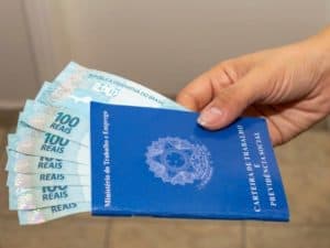 Imagem de uma carteira de trabalho com várias cédulas de 100 reais. Foto utilizada para ilustrar uma notícia sobre como solicitar o seguro-desemprego.