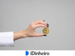 mão na horizontal, com pulso coberto por uma camisa branca, segurando uma moeda amarelada com o símbolo do gmt token fundido