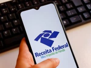 Imagem de um celular com a logo da Receita Federal. Foto utilizada para ilustrar uma notícia sobre o pagamento do 5º lote de restituição do IR 2022. Crédito: Blossom/Shutterstock