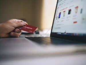 pessoa segurando um cartão de crédito e comprando nas melhores plataformas de e-commerce pelo seu laptop