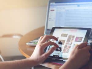 nomes para loja virtual: uma pessoa realizando compras online através de um tablet com um notebook ligado ao fundo
