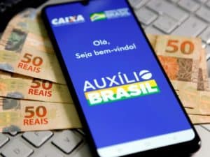 Imagem de um celular com o aplicativo do Auxílio Brasil, em cima de algumas cédulas de 50 reais. Foto utilizada para ilustrar uma notícia sobre o pagamento do auxílio brasil outubro. Crédito: Shutterstock