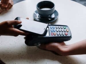 Imagem de uma pessoa pagando um café com o celular aproximando da maquininha de cartão