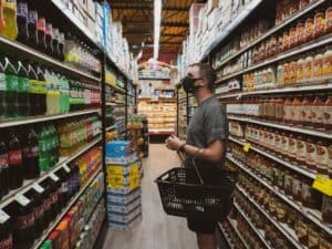 Imagem de uma pessoa com uma cesta de compras em um corredor de supermercado. Imagem utilizada para ilustrar uma notícia sobre o ipca de novembro. Crédito: Unsplash.